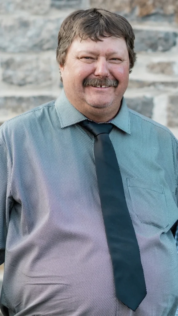 WEIBEL, Christian Weibel Smiling man wearing a tie against stone wall.