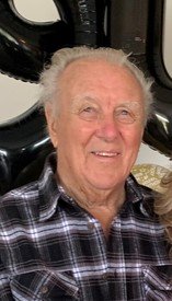 Elderly man smiling in a plaid shirt.