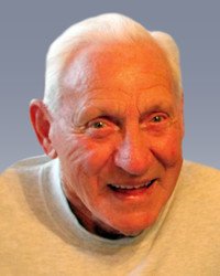 Smiling elderly man with white hair and sweater.