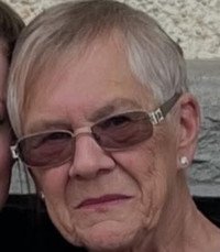 Elderly person with glasses and short hair smiling.