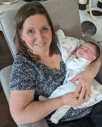 Woman smiling, holding a newborn baby.