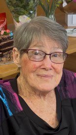 Elderly woman smiling with glasses and short hair.