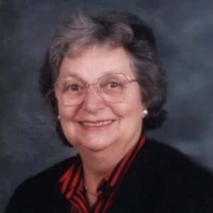 Elderly woman smiling with glasses and gray hair.