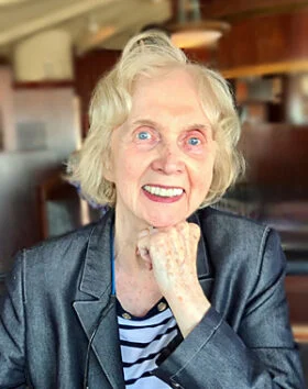 Smiling elderly woman in a blazer indoors.