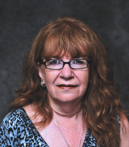 Woman with glasses, brown hair, and patterned blouse.
