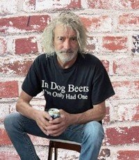Man in humorous t-shirt holding drink, brick background.