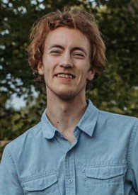 Person smiling outdoors with trees background.