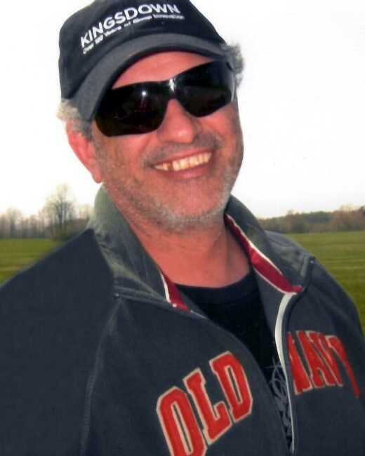 Smiling man wearing sunglasses and baseball cap outdoors.