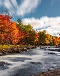 Autumn river scene with colorful foliage and clouds.
