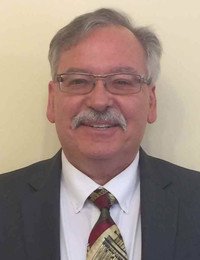 Man in suit smiling, wearing glasses and mustache.
