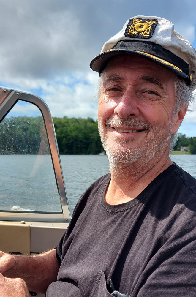 Older man smiling on a boat outdoors.