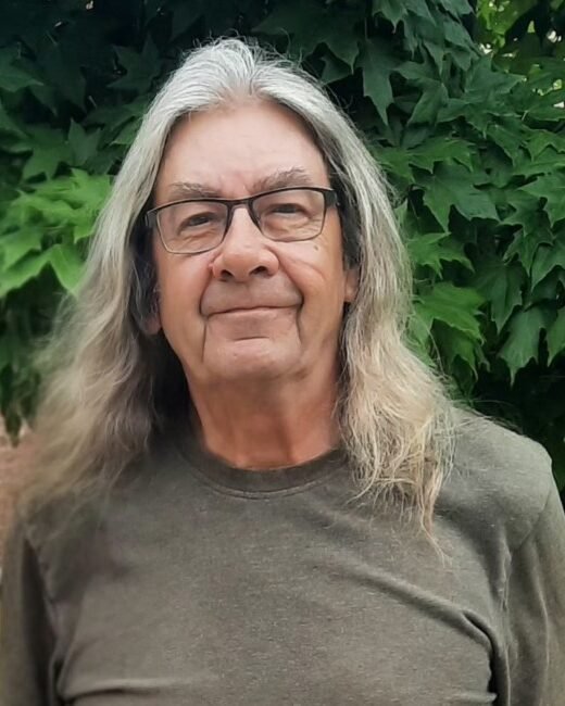 Elderly man with long hair and glasses outdoors.