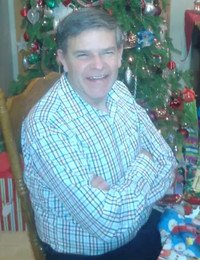 Smiling man beside Christmas tree indoors.