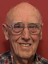 Smiling elderly man with glasses and plaid shirt.