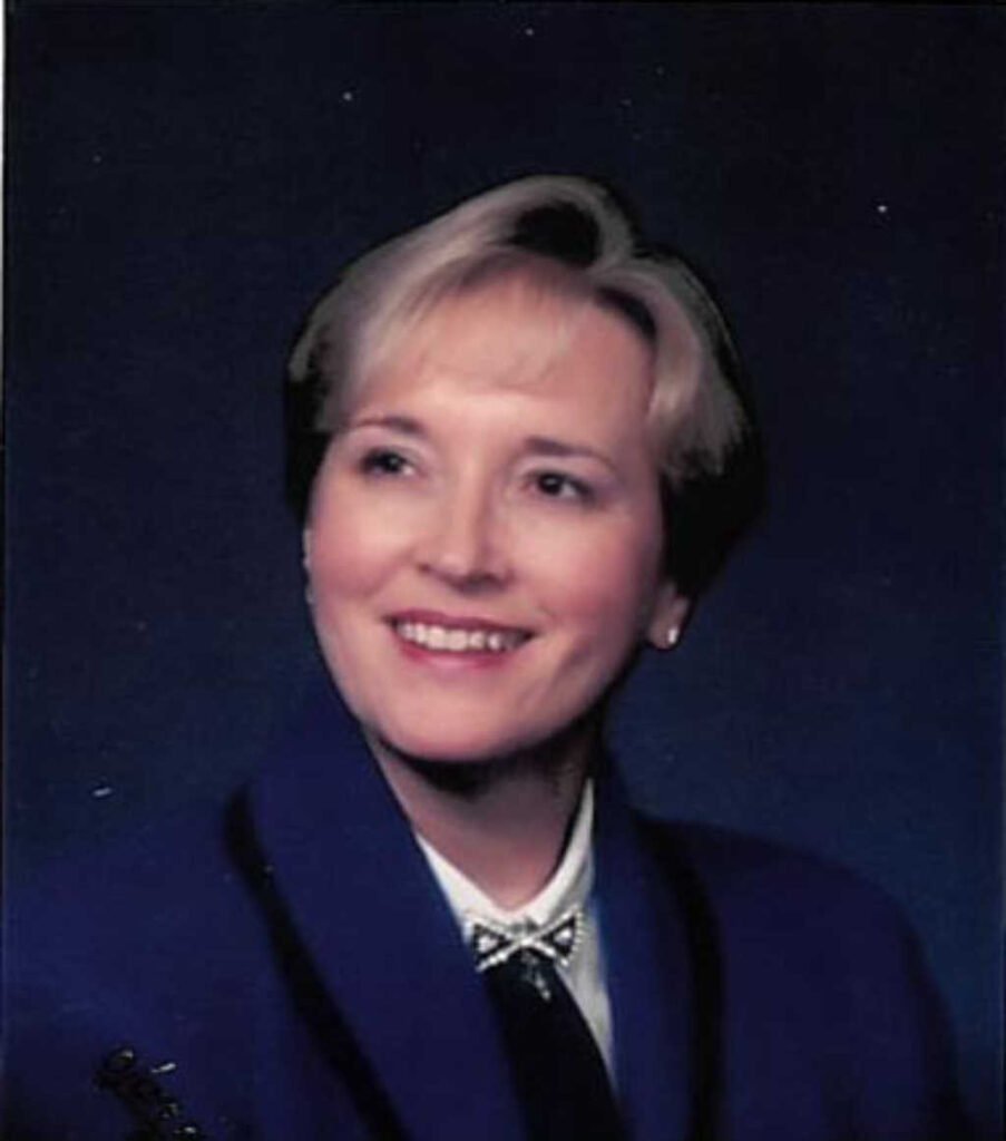 Woman smiling in professional attire, dark background.