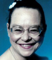 Smiling woman with glasses and floral hair accessory.