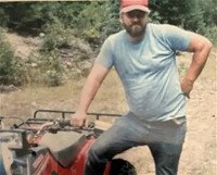 Man in cap standing beside ATV in nature.