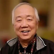 Smiling elderly person with gray hair and jacket.