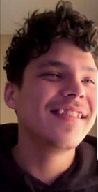 Smiling person with curly hair in a hoodie.