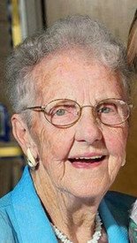 Smiling elderly woman with glasses and blue jacket.