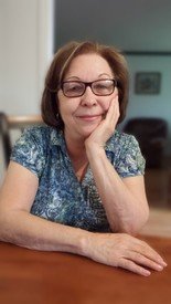 Woman smiling, wearing glasses, rests chin on hand.