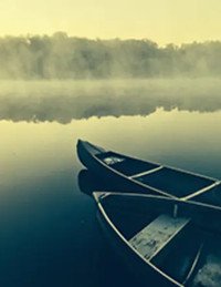 Two canoes on a misty lake at sunrise.