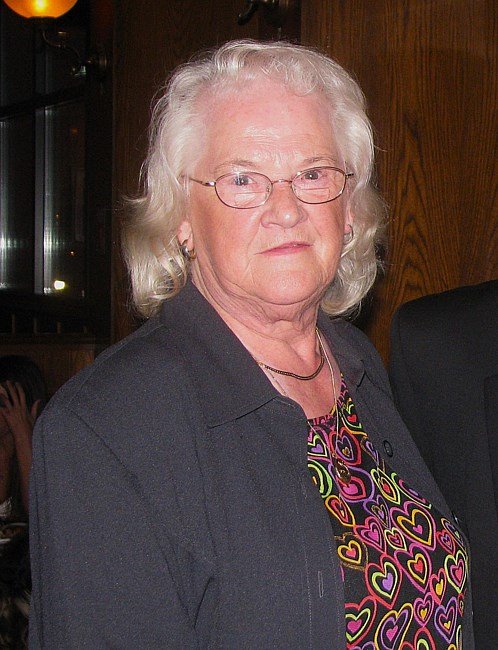 Elderly woman with glasses and colorful blouse.