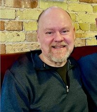 Smiling man sitting against brick wall background.
