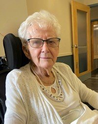 Elderly woman in wheelchair wearing glasses and sweater.