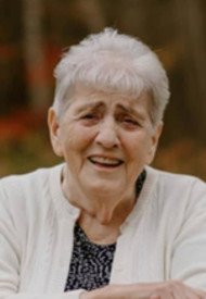 Elderly woman smiling outdoors in fall setting.