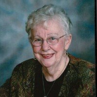 Elderly woman smiling, wearing glasses and earrings.