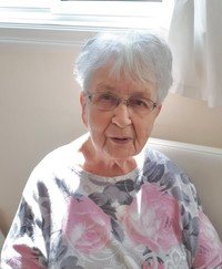 Elderly woman sitting near a window smiling.