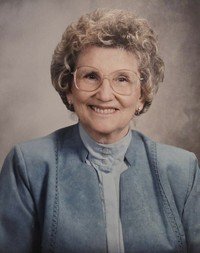 Smiling elderly woman with glasses in blue jacket.