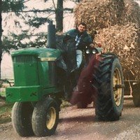 Person driving tractor with hay bales behind.