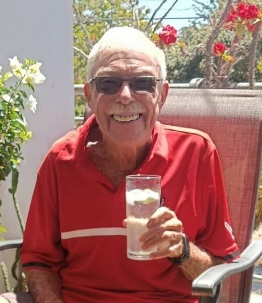 Smiling man enjoying a drink outdoors in sunlight.