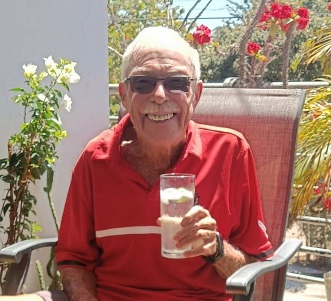 Smiling man enjoying a drink outdoors in sunlight.