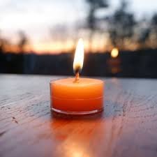 Lit candle on wooden table at sunset.