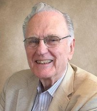 Smiling elderly man in beige suit and glasses.