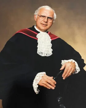 Elderly man in judicial robe and wig.