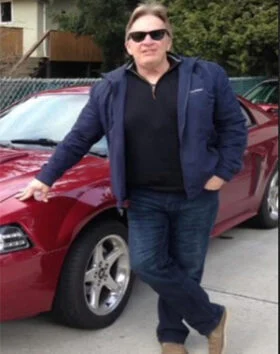 Person standing by a red car, wearing sunglasses.