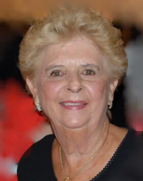 Smiling elderly woman with short hair, formal attire.
