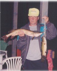 Man holding two large fish at night.