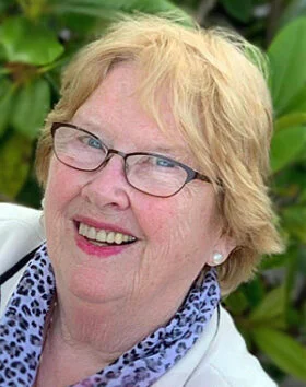 Smiling elderly woman outdoors with glasses and scarf.