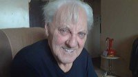 Elderly man smiling in cozy room setting.
