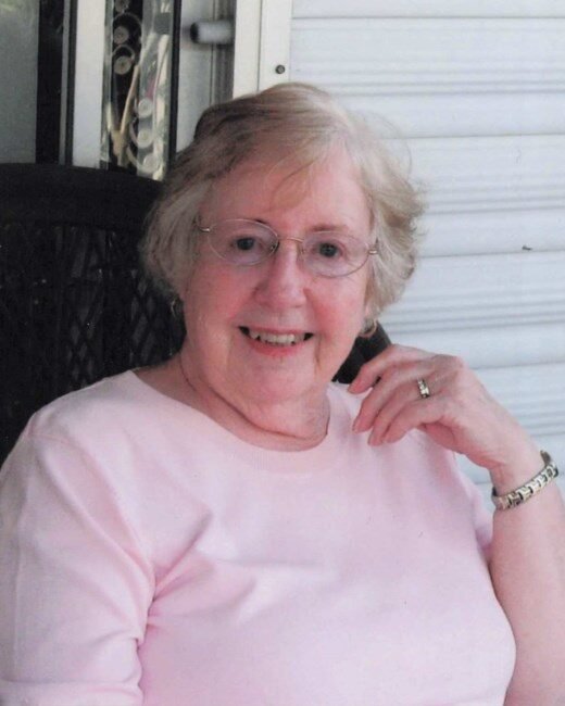 Smiling woman sitting on porch in pink shirt.