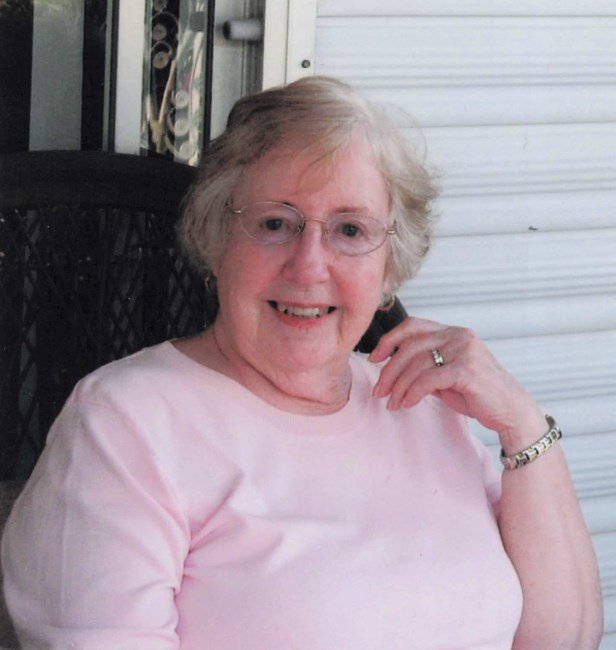 Smiling woman sitting on porch in pink shirt.