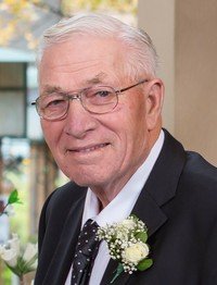 Elderly man in suit with boutonniere smiling.