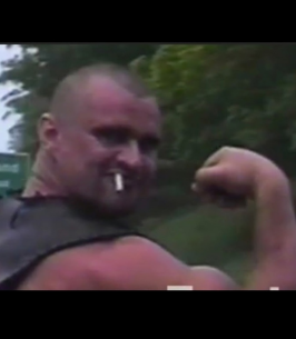 Man flexing arm with a cigarette outdoors.