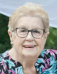 Elderly woman with glasses smiling outdoors.
