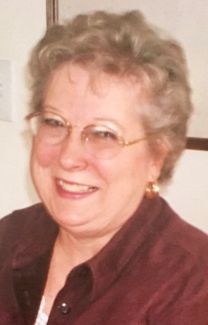 Smiling person wearing glasses and a brown jacket.